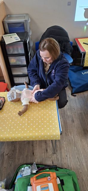A nursery practitioner practising infant CPR with an AED and response bag ready